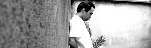 Photo of a man in a white shirt leaning with his back against a wall